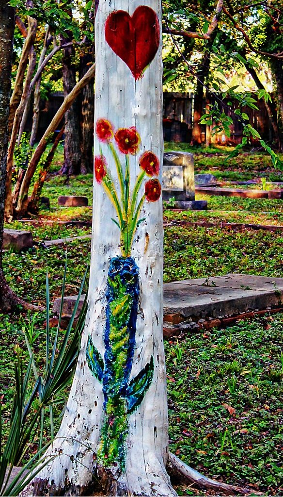 Tree trunk painted white with a red heart and a bouquet of orange flowers coming out of a blue vase.