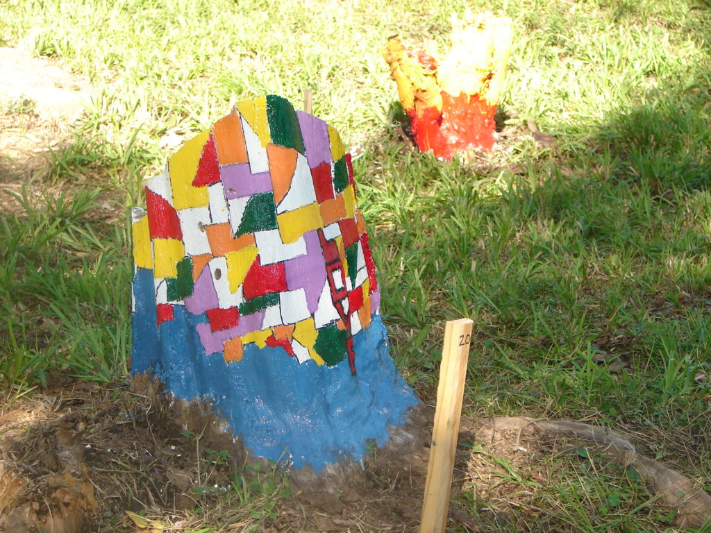 Tree stump painted a mosaic of colors in various geometric shapes with a light blue base.