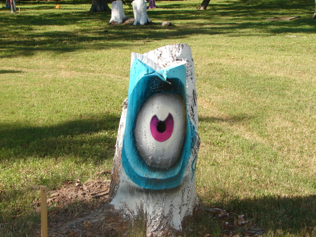 Tree stump painted to look like an eye with a teal socket and a pink iris.