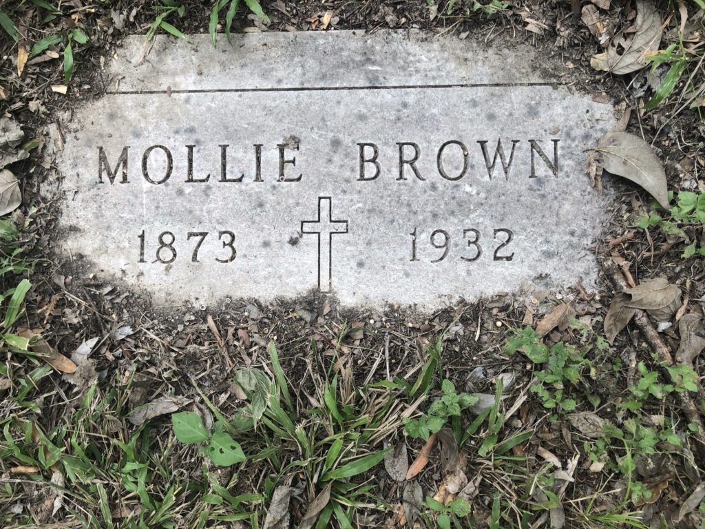 Small gray headstone surrounded by dirt on the edges, says "Mollie Brown; 1873" cross "1932."